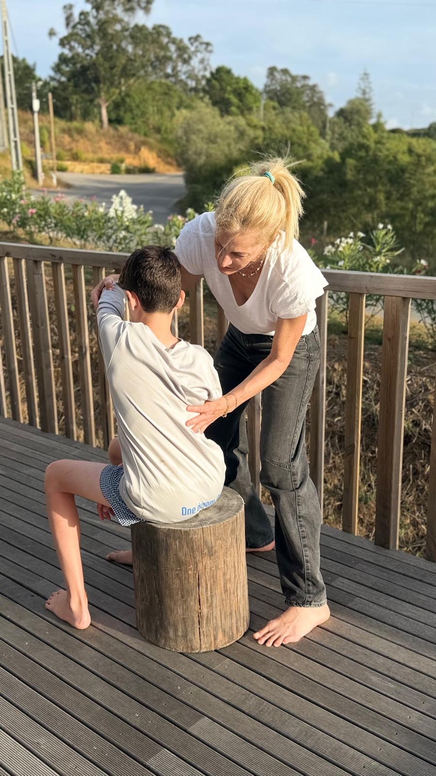 Naomi guiding the back and shoulder of a young person seated on a wooden stump