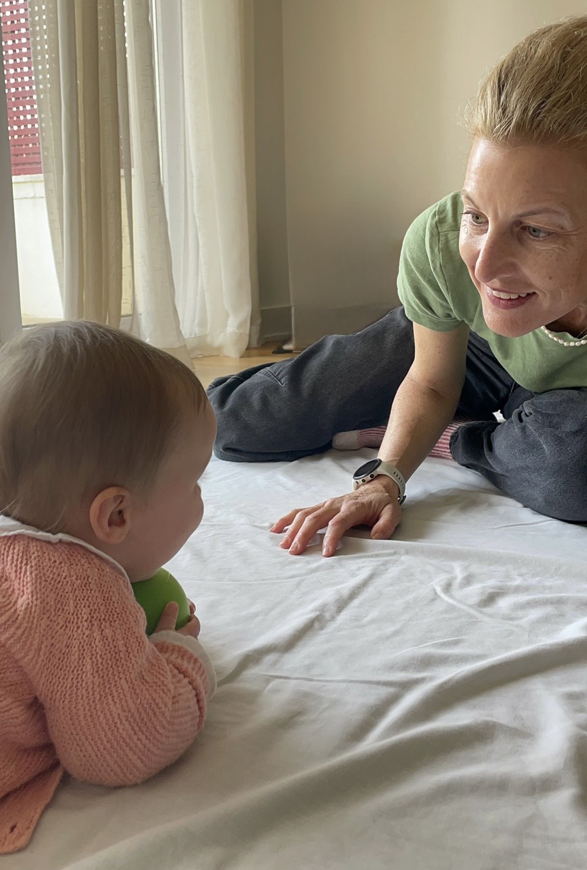 Naomi lying on the floor at eye level with a baby, sharing attention over a green ball