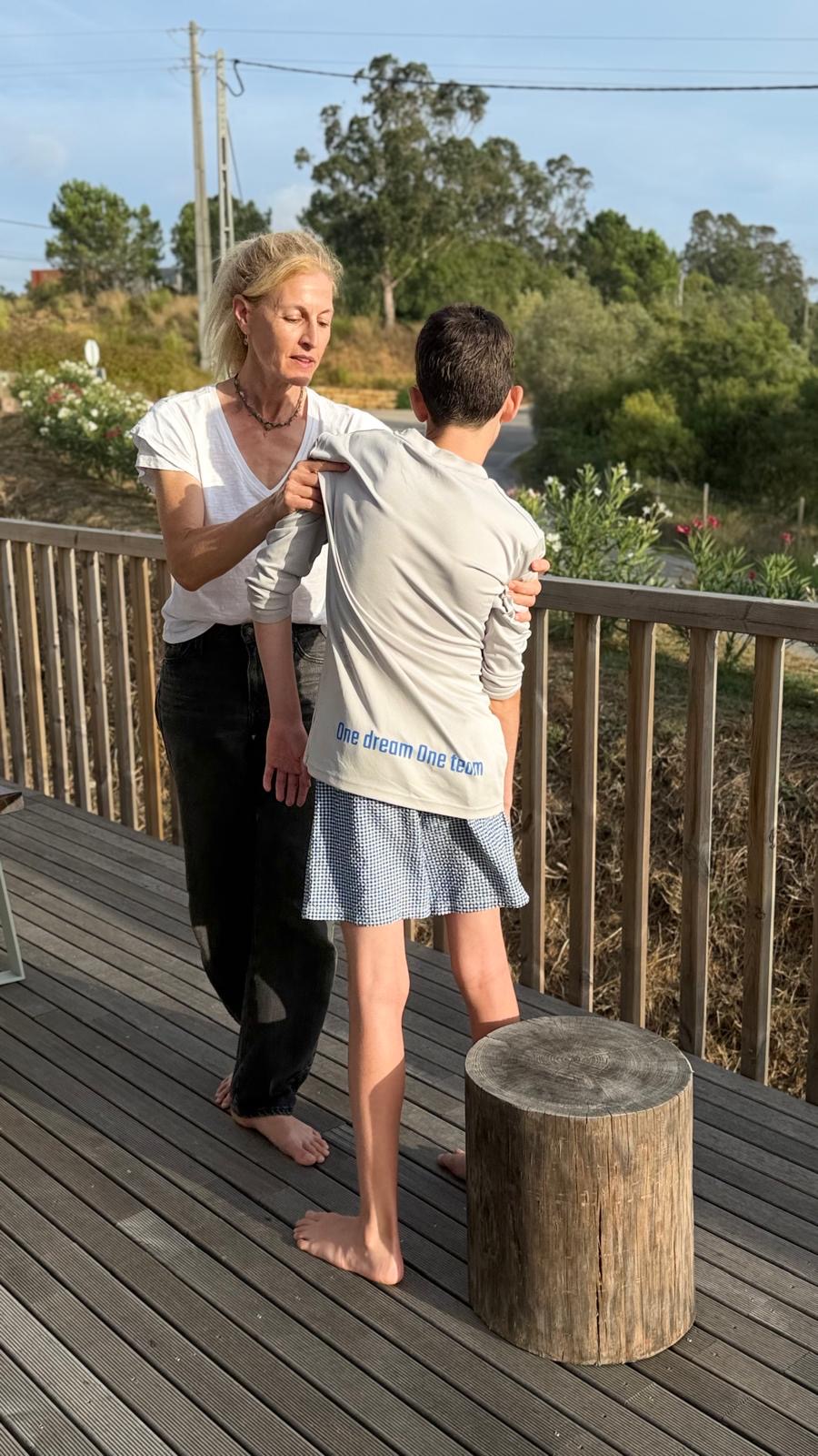 Naomi guiding a standing person's shoulders as they balance on a wooden stump